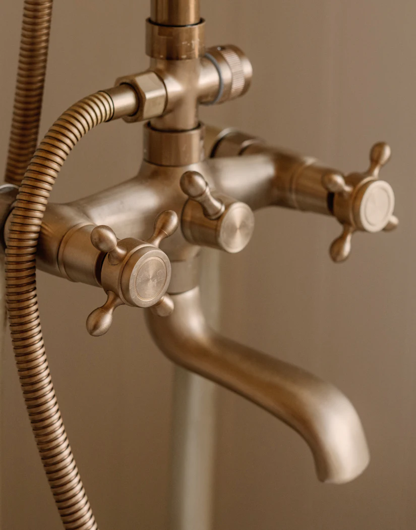 Close-up of a brushed brass shower mixer with cross-head handles and a curved spout